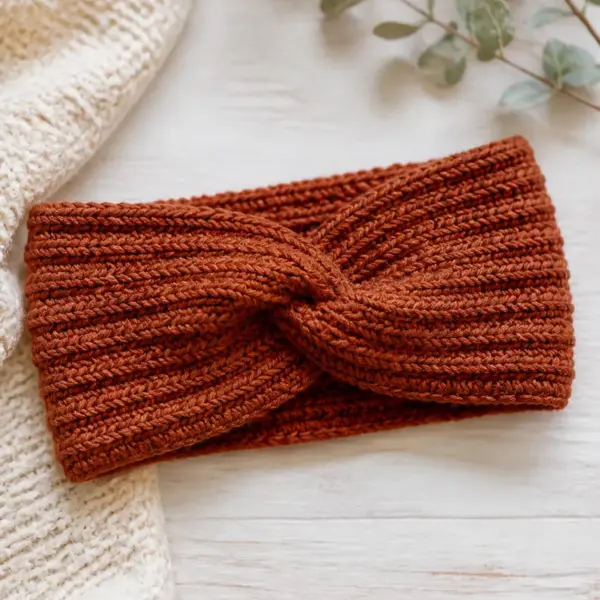 Finished warm rust ribbed ear warmer with a subtle front twist photographed in natural daylight