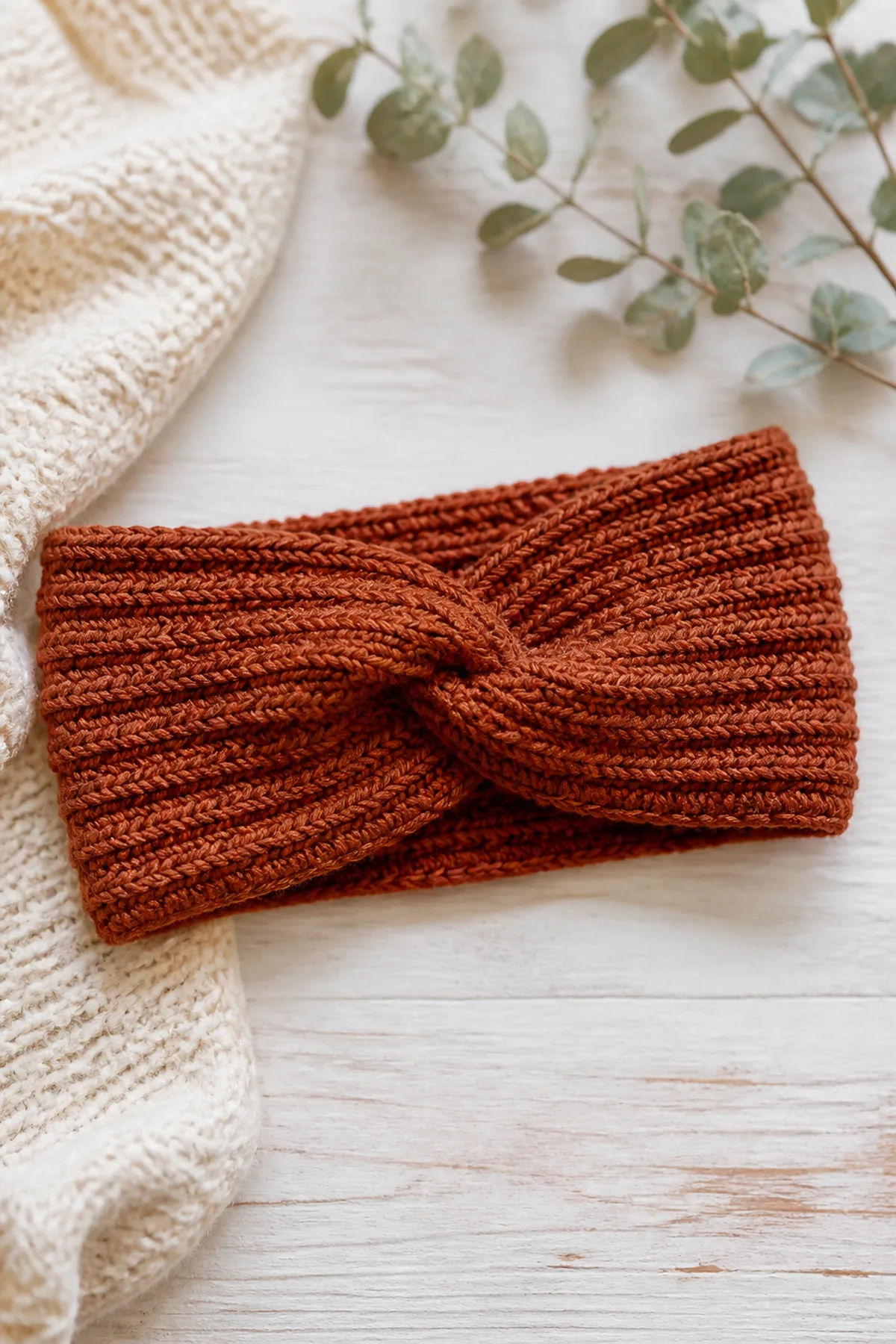 Finished warm rust ribbed ear warmer with a subtle front twist photographed in natural daylight